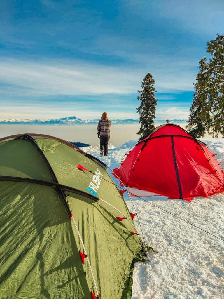 A person enjoys a snowy mountain view with tents set up, under a clear blue sky.